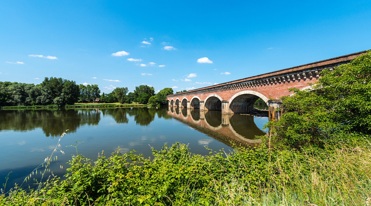 red brick bridge over blue canal water with blue sky and white clouds
